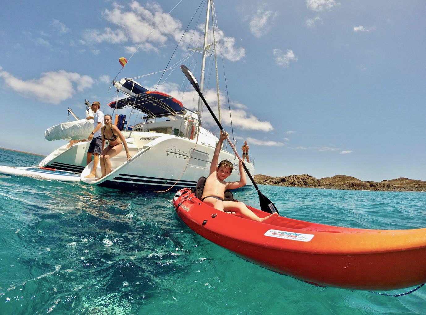 Una pequeña familia disfrutando en el agua y en un kayak durante su excursión en un catamarán de alquiler privado.